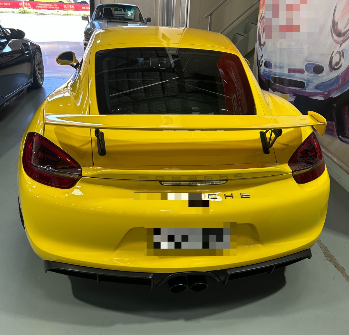 A Porsche Cayman GT4 in racing yellow, photographed by us; number plate blurred per our privacy policy. Photography: Queen of Cars.